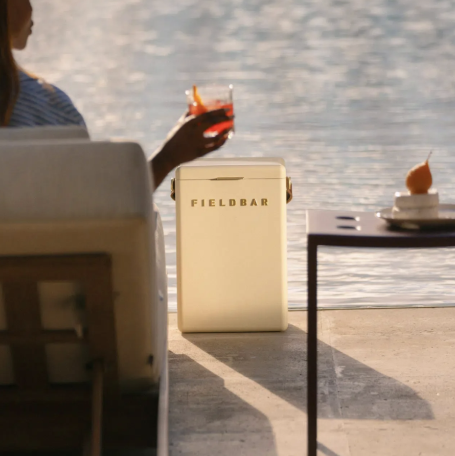 A cream Fieldbar cooler box beside the water as a guest raises a cocktail