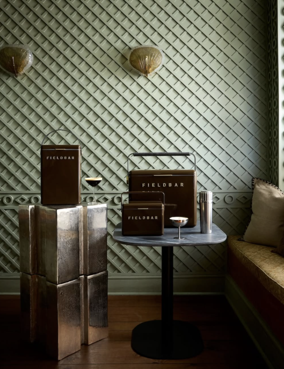 Three brown Fieldbar cooler boxes staged in a green-panelled lounge with cocktails