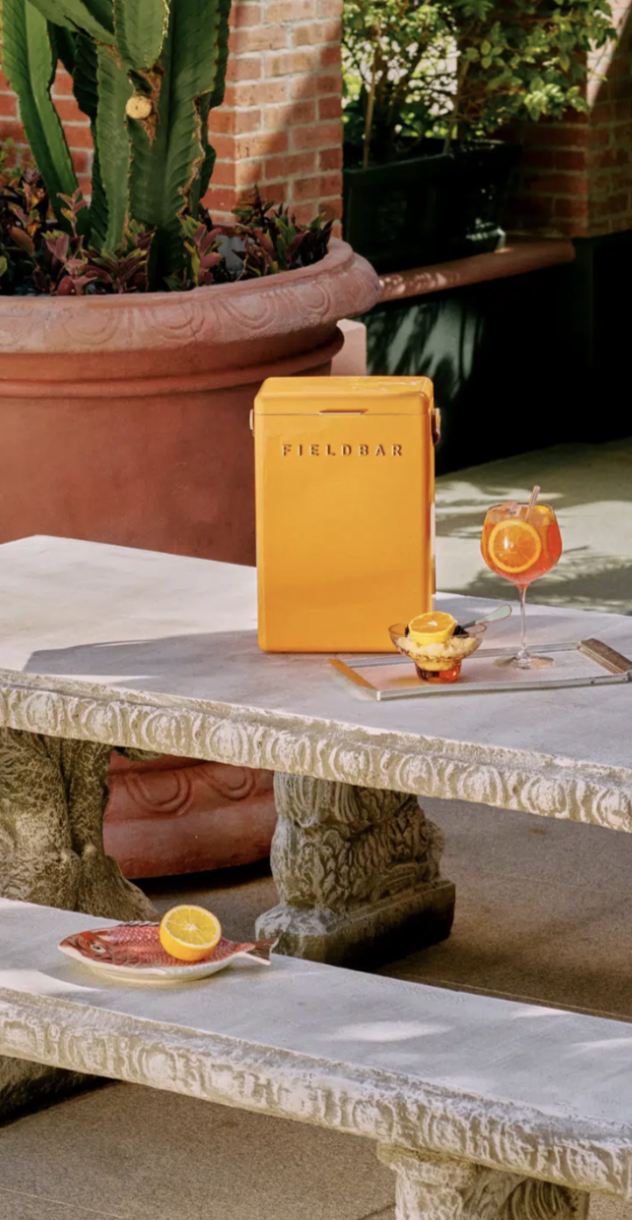An orange Fieldbar cooler on a stone table with a spritz and citrus