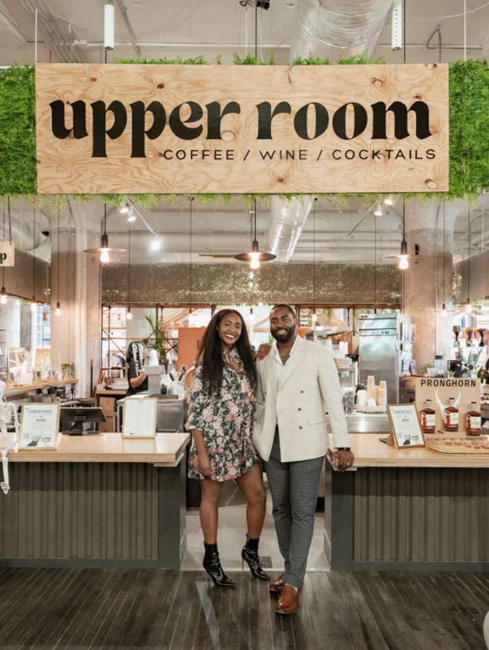 The owners of the Upper Room standing beneath the venue's signature sign
