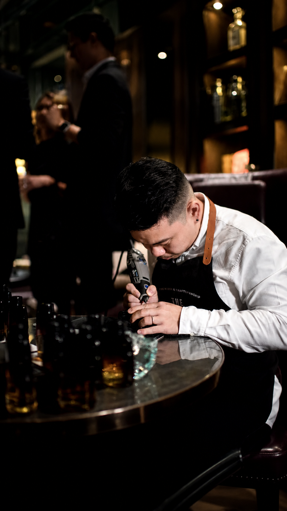 A craftsman engraving a bottle by hand at a candlelit table