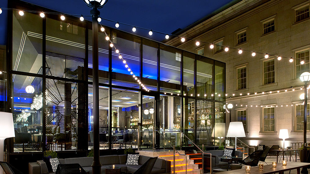 A dim hotel cocktail bar with a single Manhattan under a brass pendant