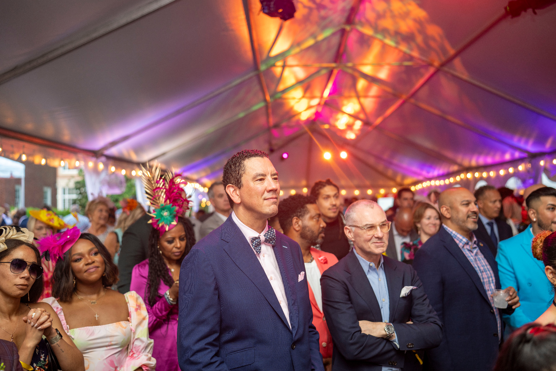 A tented Preakness crowd in tailored color under string lights