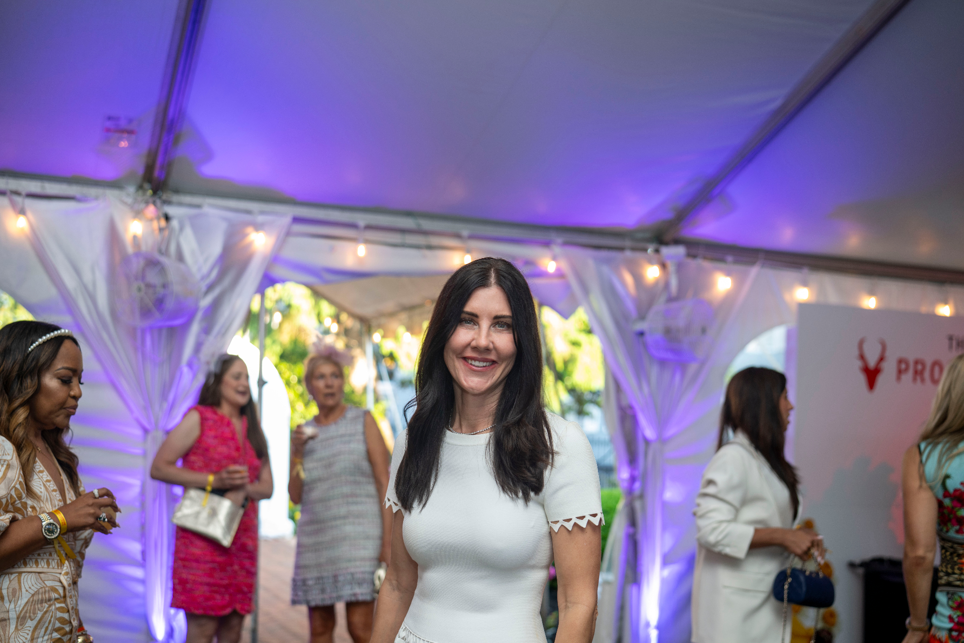 A guest in white amid soft purple light and string-lit tenting